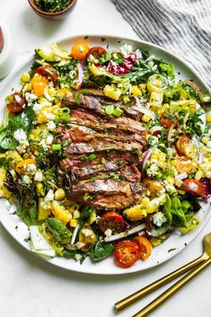 a plate with steak and salad on it next to some gold utensils in small bowls