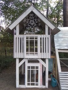 a white wooden house with windows and a balcony on the top floor in front of some trees