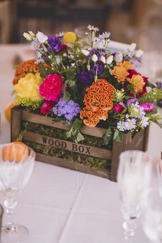 a wooden box filled with colorful flowers on top of a white tablecloth covered table