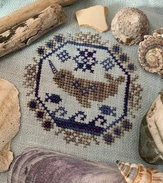 some seashells and other items on a blue cloth with a cross - stitch pattern