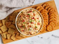 a bowl of dip surrounded by crackers on a cutting board