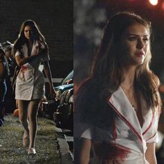 a woman in white dress walking down the street at night and onlookers