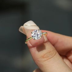 a woman's hand holding a diamond ring on top of a flower shaped object