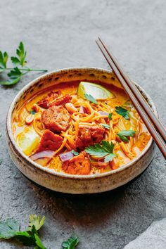 a bowl filled with noodles, meat and veggies next to chopsticks