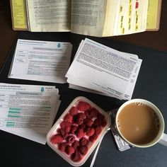 there is a container of raspberries next to a cup of coffee and an open book