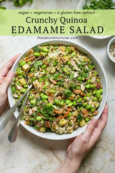 two hands holding a white bowl filled with edamame salad on top of a marble table