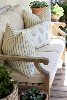 a couch with pillows and some plants on the back porch area in front of a house