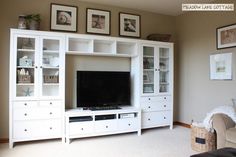 a white entertainment center in a living room with pictures on the wall above and below it