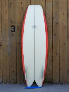 a red and white surfboard leaning against a wooden fence