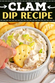 a hand dipping crackers into a dip in a white bowl with crackers on the side