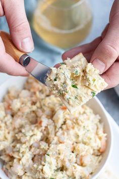 two hands holding a knife over a white bowl filled with rice and vegetables, ready to eat