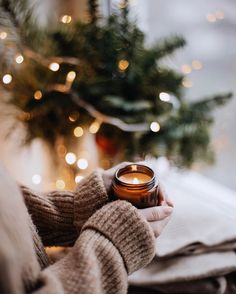 a person holding a candle in their hand near a christmas tree and lights on the window sill