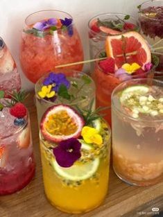 many different types of drinks on a wooden table with flowers and fruit in them,