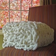 a large chunky blanket sitting on top of a chair next to an open window