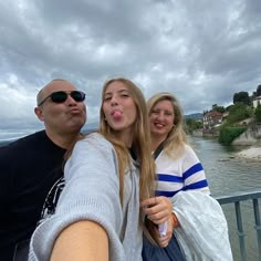 two women and a man taking a selfie on a bridge over the water with houses in the background