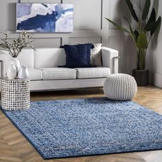 a living room with white couches, blue rug and large painting on the wall