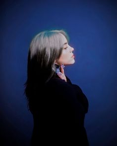 a woman is talking on her cellphone while standing against a dark blue background,