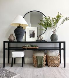 a black console table with two vases and a mirror on it, next to a white chair