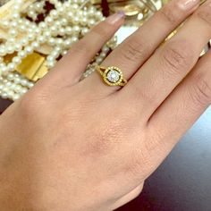 a woman's hand with a diamond ring on top of her finger and pearls in the background