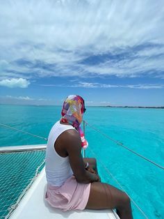 a woman sitting on the back of a boat in clear blue water with clouds overhead