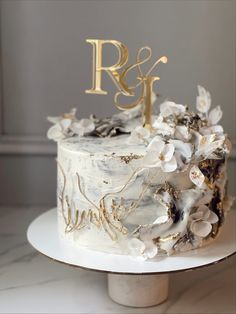 a white cake with gold letters and flowers on the top is sitting on a table