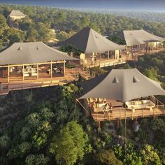 an aerial view of several large tents in the jungle with trees surrounding them and people standing outside