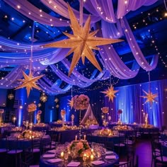 a large room with many tables and chairs covered in white draping, stars hanging from the ceiling