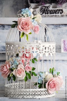 a white birdcage with pink roses and blue flowers on the inside is sitting on a table