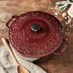 a red pot sitting on top of a wooden table next to a spatula and spoon