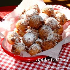 powdered sugar covered donuts in a red bowl on a checkered tablecloth