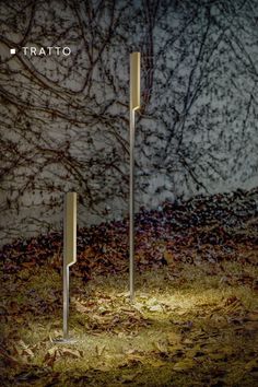 two tall metal poles in the grass with trees behind them and text that reads tratto