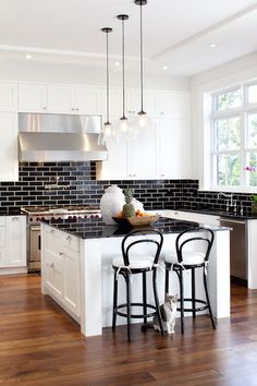 a kitchen with black and white tile backsplash, wooden flooring and bar stools