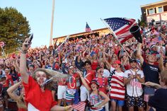 a large group of people at a sporting event waving american flags and holding their hands in the air