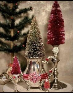 three christmas trees are sitting on a table next to silver dishes and cups with red decorations