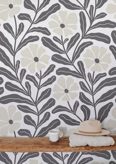 a hat and cup on a shelf in front of a wallpapered background with leaves