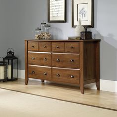 a wooden dresser with two framed pictures on the wall and a lamp next to it