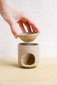 a hand is picking up a small bowl from the top of a ceramic cup on a table