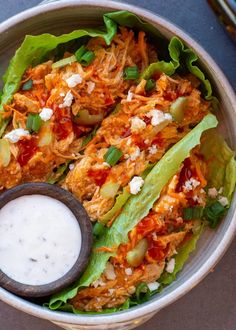 a bowl filled with lettuce and meat next to a small container of ranch dressing