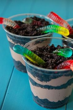 two plastic cups filled with dirt and toothbrushes sitting on top of a blue table