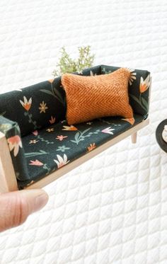 a miniature couch with a pillow on it in someone's hand next to a bed