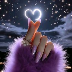 a woman's hand with purple nail polish holding a heart shaped object in the night sky