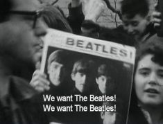 a group of people holding up signs with the beatles on them and an advertisement in front