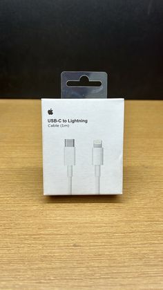 an apple charger with two usb cables in the packaging on a wooden table next to a black wall