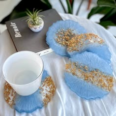 three blue and gold coasters on top of a white table cloth with a plant in the background