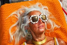 an older woman with white hair and sunglasses laying on a beach towel in the sun