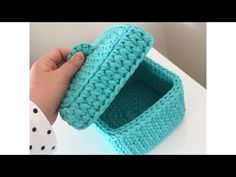 a hand is holding a crocheted box on top of a white table with polka dots