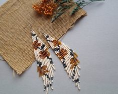 two beaded earrings sitting on top of a piece of burlock next to flowers