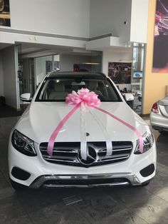 a white car with a pink ribbon tied to it's hood in a showroom