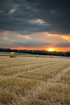 a field with hay bales in the foreground as the sun sets behind it