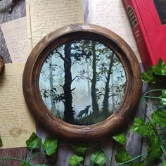 an image of a forest scene through a round window with leaves and books around it